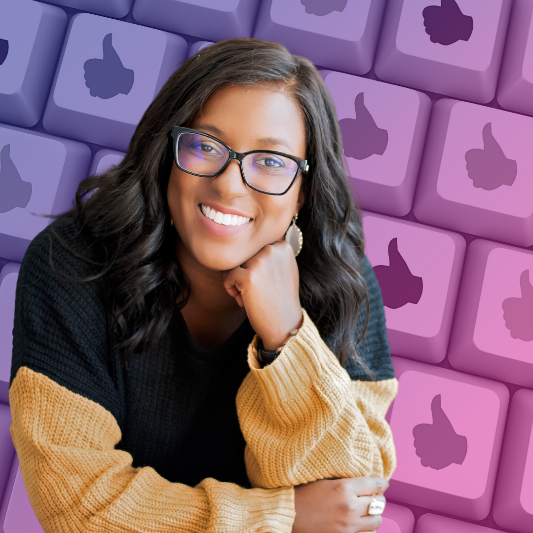 Andréa Jones is smiling at the camera and resting her chin on her hand. She's wearing black framed glasses with a black and orange sweater. In the background is a keyboard and every key is a thumbs up.