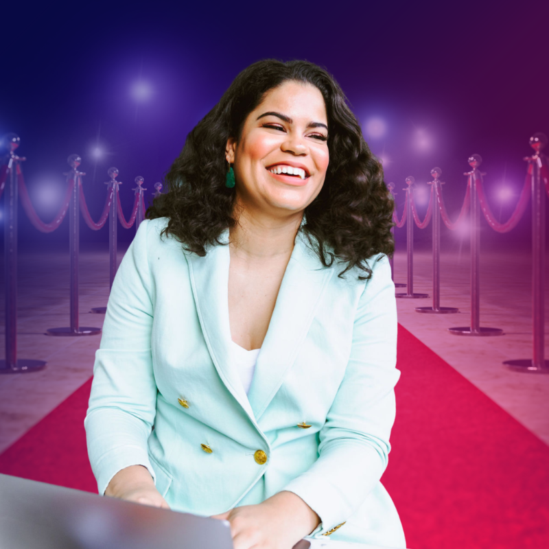 Jordan Gill is smiling in a beautiful sea-foam green suit. The background is a red carpet and there are bursts of light indicating cameras are snapping away.