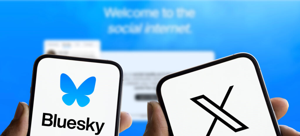 A cell phone in one hand displays the Bluesky app logo. A cell phone in another hand displays the X app logo. The background is blurred.